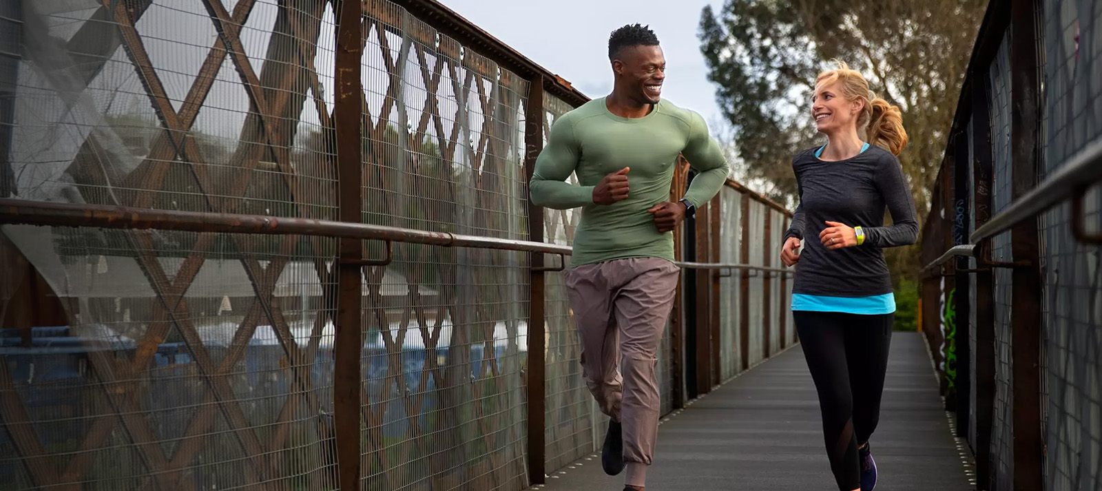 Two individuals jogging on a bridge with a backdrop of a cityscape.