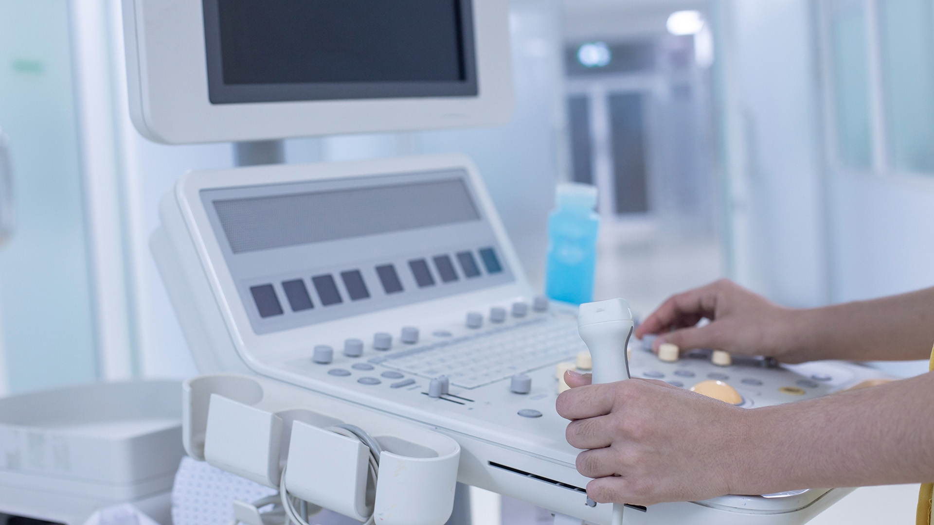 A person sitting at a computer with a medical device behind them.