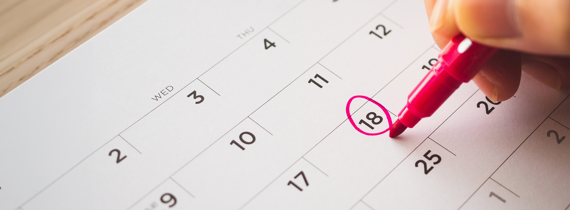 A close-up photo of a hand writing on a calendar, with a pink highlighter pen marking the 10th day of the month.