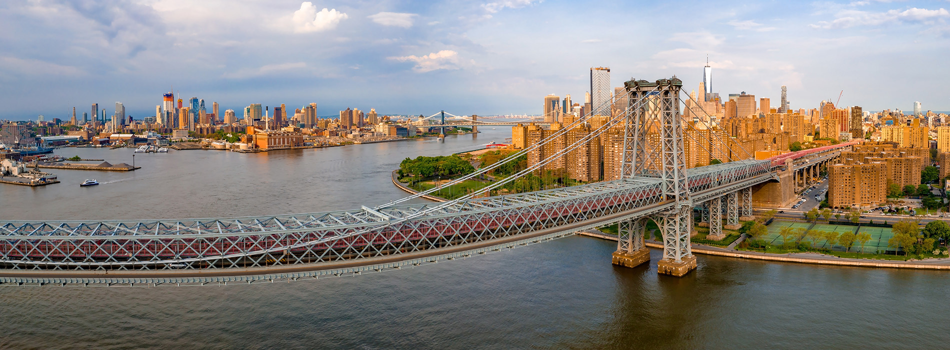 The image shows a panoramic view of a city skyline with a river running through it, featuring two bridges, a prominent skyscraper, and a clear sky.