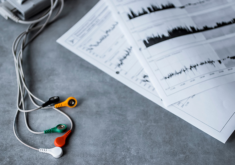 The image features a pair of earbuds with a smartphone charger cable connected to them, resting on a table next to a piece of paper with graphs and charts.