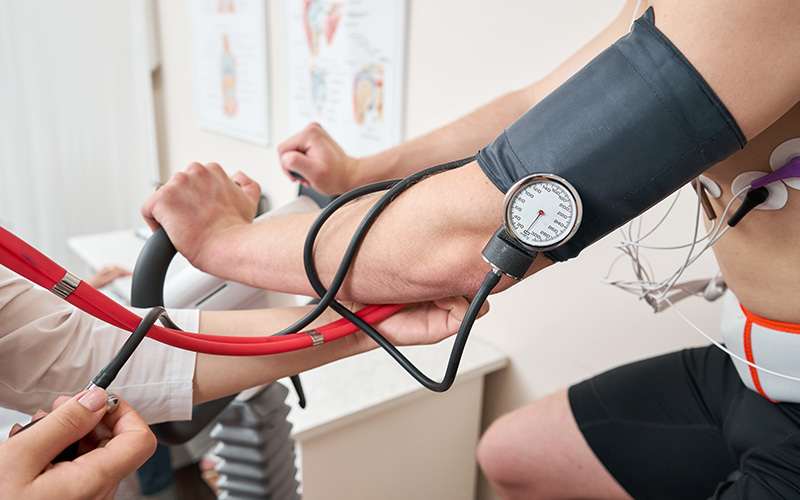 A person taking a blood pressure reading with a cuff around an arm while another individual monitors the process.